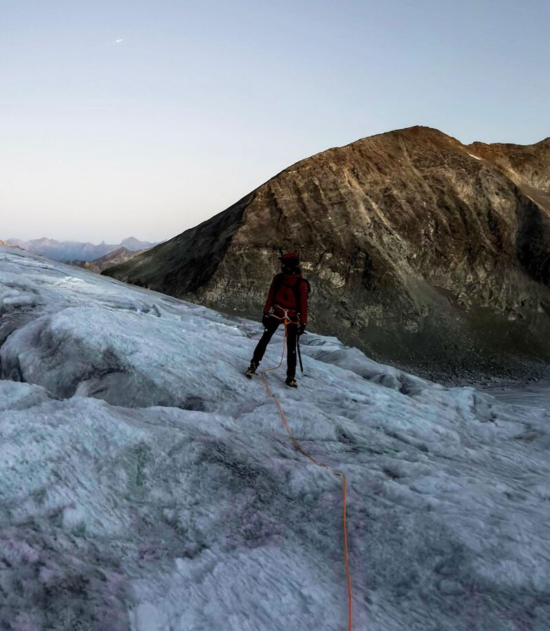 Lucien, de dos, encordé sur un glacier à l'aube.